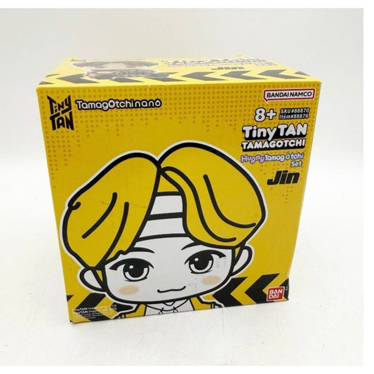 Bright yellow product box for Tiny TAN Tamagotchi featuring cartoon character Jin with blonde hair and striped headband, Bandai Namco branding visible.