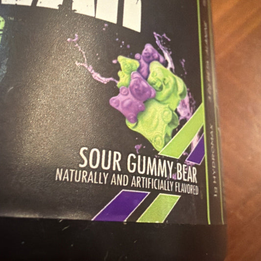 Close-up of black product packaging showing purple and lime-green gummy bears with "Sour Gummy Bear" text and flavor description.