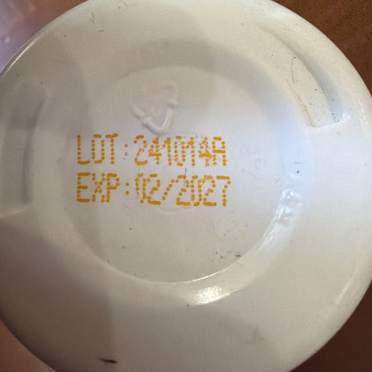 Close-up of white capsule bottle bottom showing orange printed lot number 24MM4A and expiration date 02/2027.