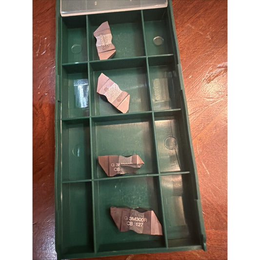 Green plastic storage case with compartments holding four brown carbide inserts labeled with product codes, viewed from above.
