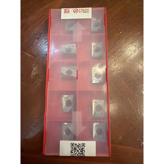 Red plastic storage case containing multiple metallic carbide inserts arranged in compartments, labeled Haas F1 Team, photographed from above.