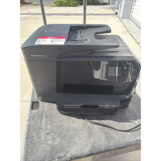HP OfficeJet Pro 8710 black multifunction printer photographed from above on concrete driveway, showing top feeder tray and control panel.