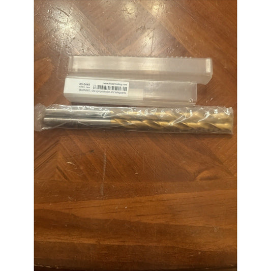 Unboxed carbide end mill drill bit with gold coating in clear plastic sleeve next to white cardboard box labeled 03-2448 on wooden surface.