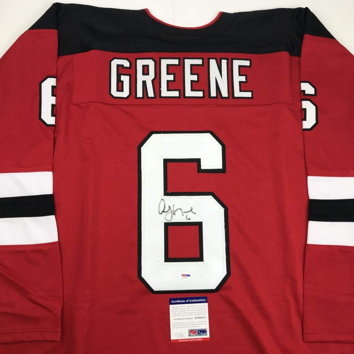 Red hockey jersey with black and white stripes displaying "GREENE" nameplate and number 6 with handwritten signature and PSA/DNA authenticity certificate.