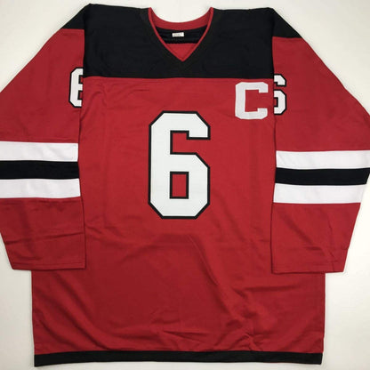 Red hockey jersey with black and white horizontal stripes on sleeves, white number 6 on chest, displayed flat against white background.