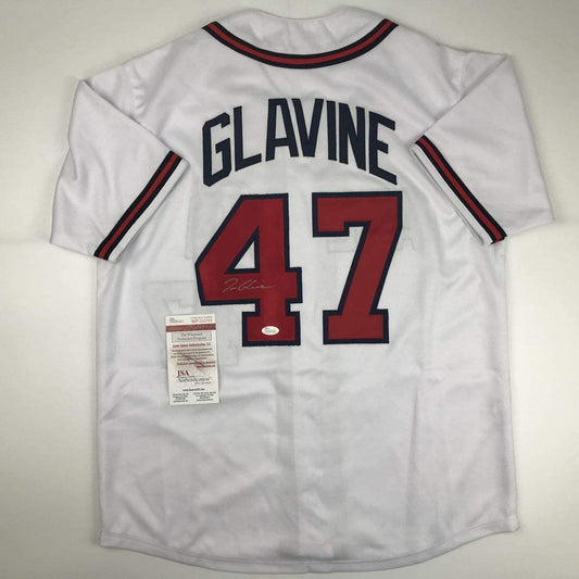 Back view of white baseball jersey displaying "GLAVINE" and number 47 in red and navy with JSA authentication label attached.