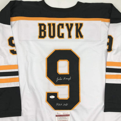 White Boston Bruins hockey jersey with black number 9, "BUCYK" nameplate, and autographed inscription including "HOF 1981" with JSA authentication label visible.