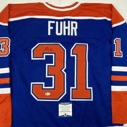 Back view of blue Edmonton Oilers hockey jersey number 31 with "FUHR" name and autographed signature, Beckett authentication sticker visible.