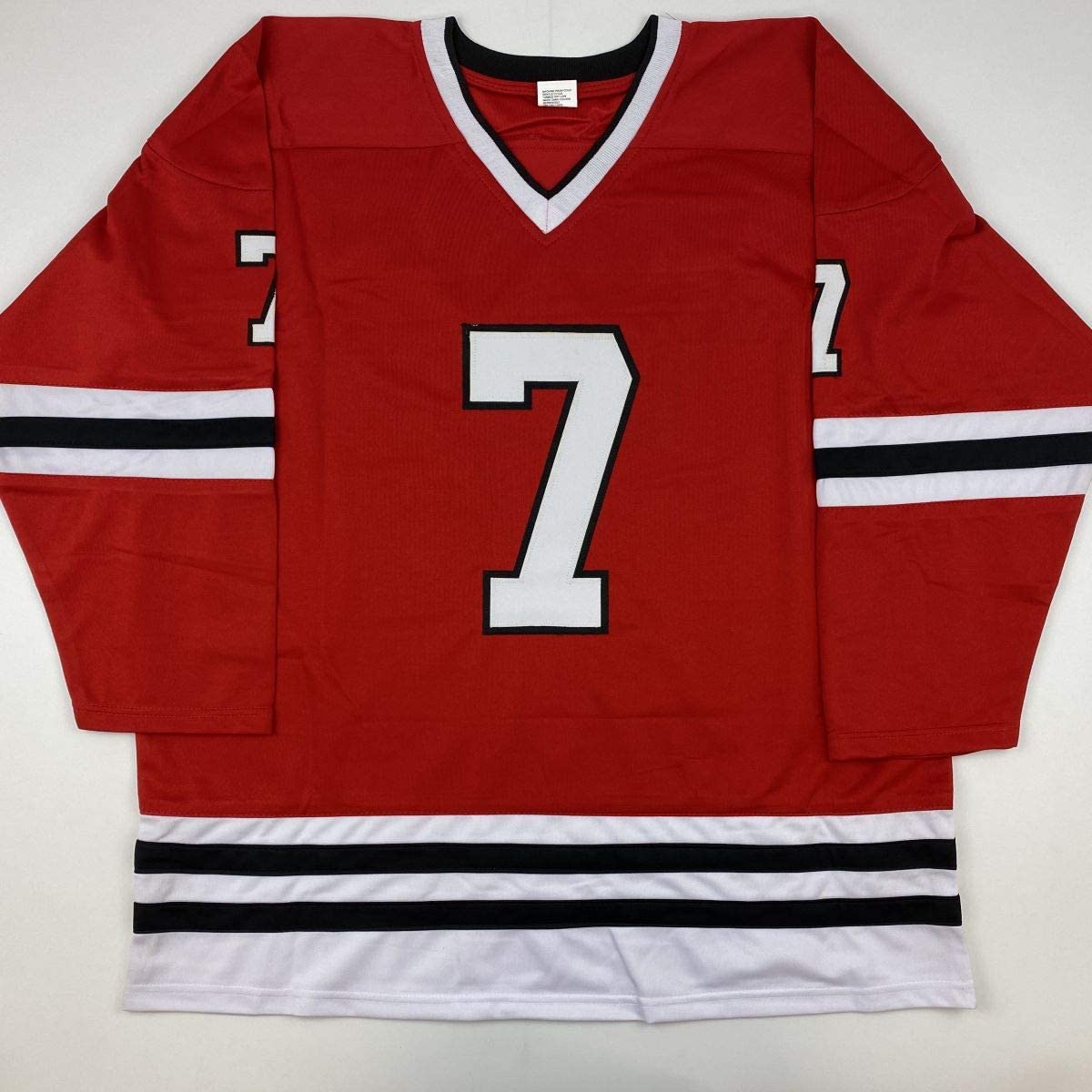 Red hockey jersey with white number 7 and black-white striped sleeves displayed flat against white background.