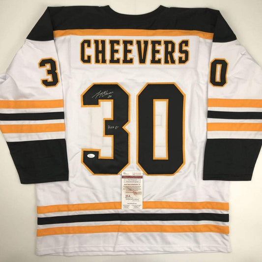 Reverse view of white Cheevers #30 Boston hockey jersey with black and orange stripes, displaying autograph and JSA authentication certificate.