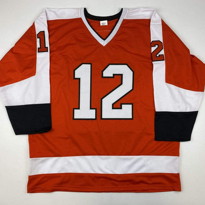 Red, white, and black hockey jersey with number 12 displayed flat against white background, front view.