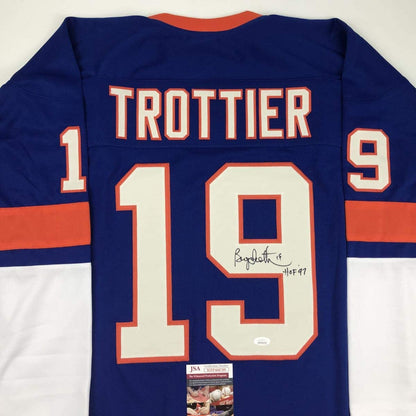 Back view of navy blue hockey jersey with "TROTTIER" and number 19 in cream and orange, signed in black ink with "HOF 97" notation, JSA authentication label visible at bottom.
