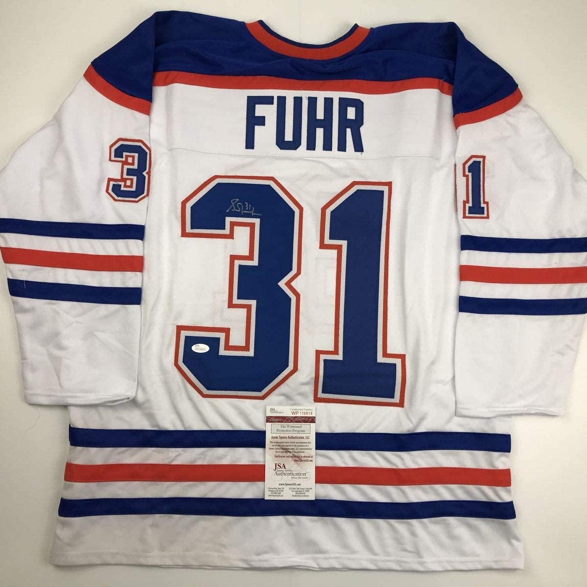 White Edmonton Oilers hockey jersey #31 with "FUHR" nameplate, navy and red stripes, displayed flat with JSA authentication certificate visible.