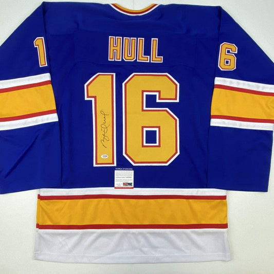 Flat lay of blue St. Louis hockey jersey number 16 with "HULL" nameplate, signed, showing front with yellow and red stripes.