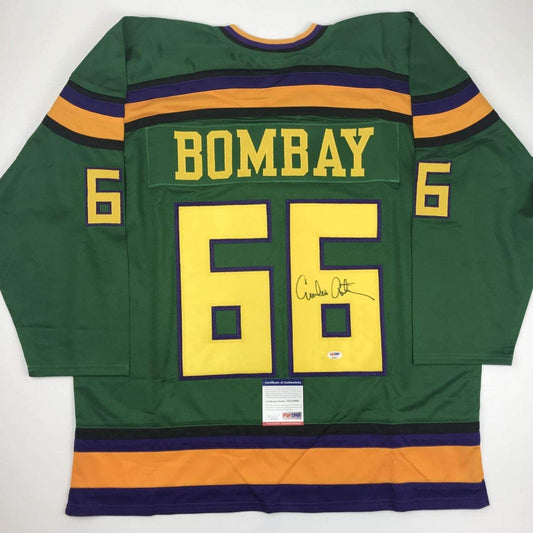 Green hockey jersey with "BOMBAY" and number 55 in yellow, featuring navy and gold stripes, displayed flat with PSA/DNA authentication certificate visible at bottom.