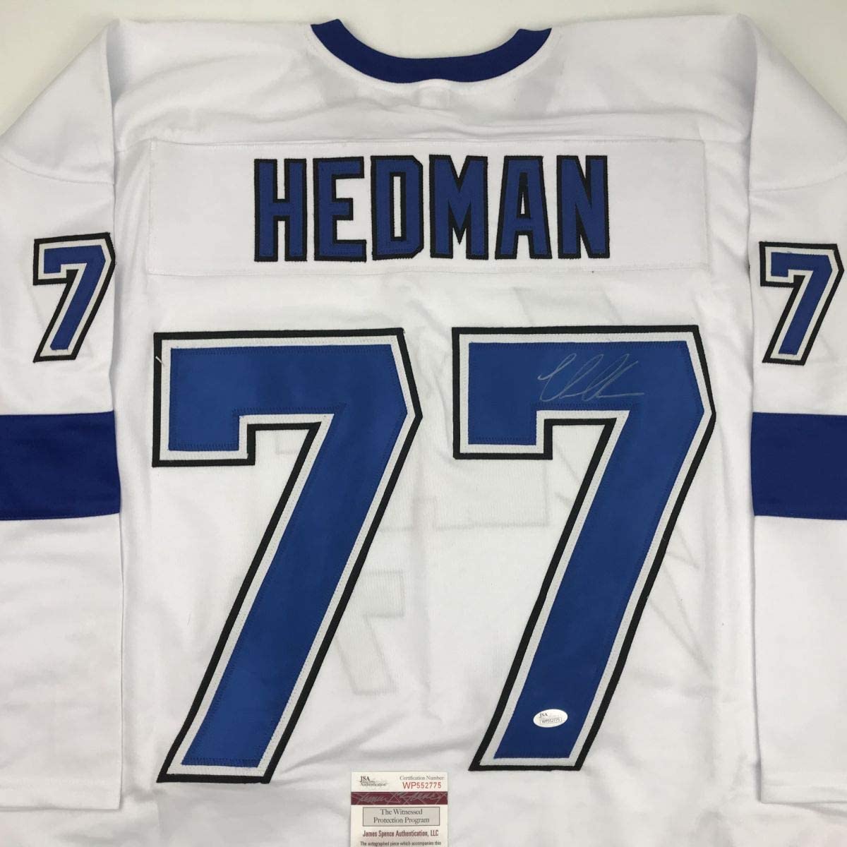 White hockey jersey with blue number 77, "HEDMAN" name plate, and JSA authentication label visible on front.