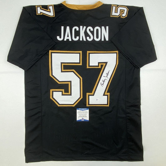 Black New Orleans Saints football jersey number 57 with "JACKSON" nameplate, gold and white trim, displayed flat with Beckett authentication certificate visible.