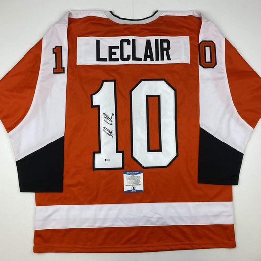 Back view of orange and white Philadelphia Flyers hockey jersey number 10 with LeClair nameplate and signature, Beckett authentication sticker visible.