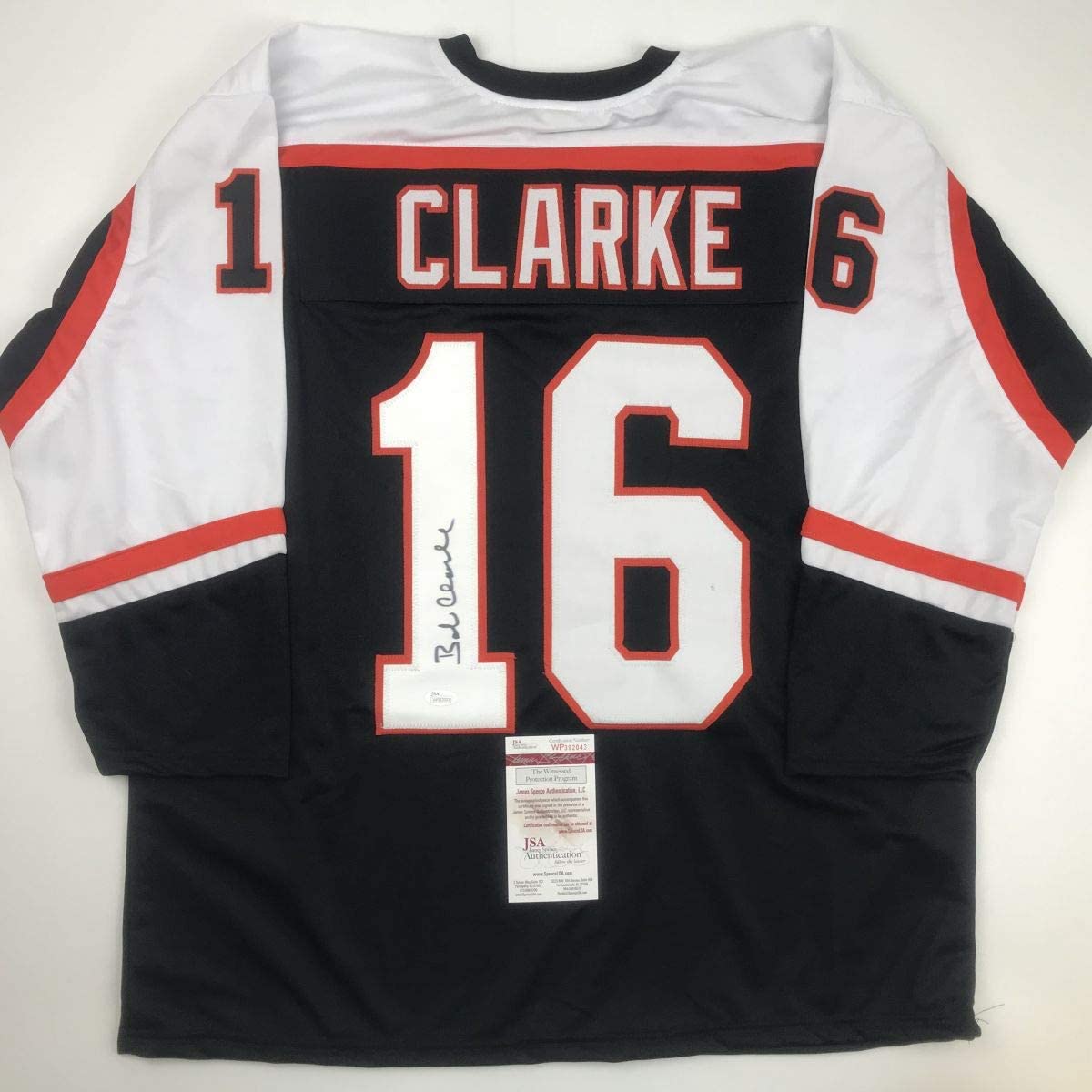 Signed black Philadelphia Flyers hockey jersey number 16 with Clarke nameplate displayed flat, showing JSA authentication certificate.