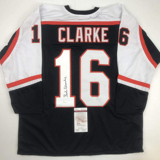 Signed black Philadelphia Flyers hockey jersey number 16 with Clarke nameplate displayed flat, showing JSA authentication certificate.