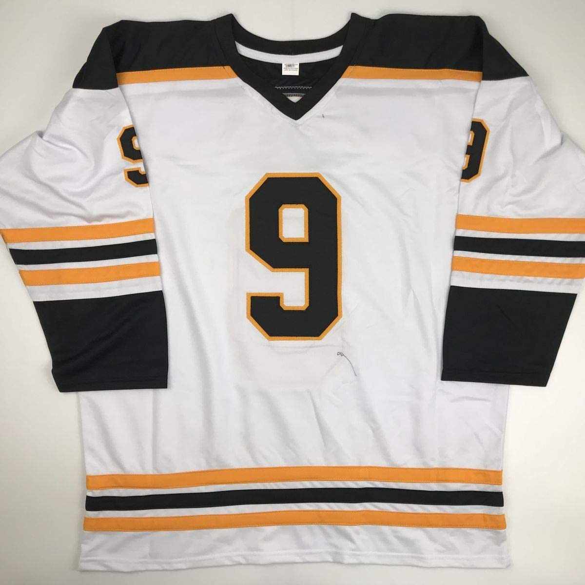 White hockey jersey with black and orange stripes, number 9 in black and orange on chest, displayed flat against neutral background.