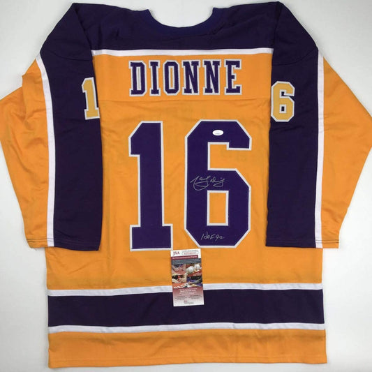 Flat lay of signed yellow and navy LA Kings hockey jersey number 16 with "DIONNE" nameplate and JSA authentication certificate attached.