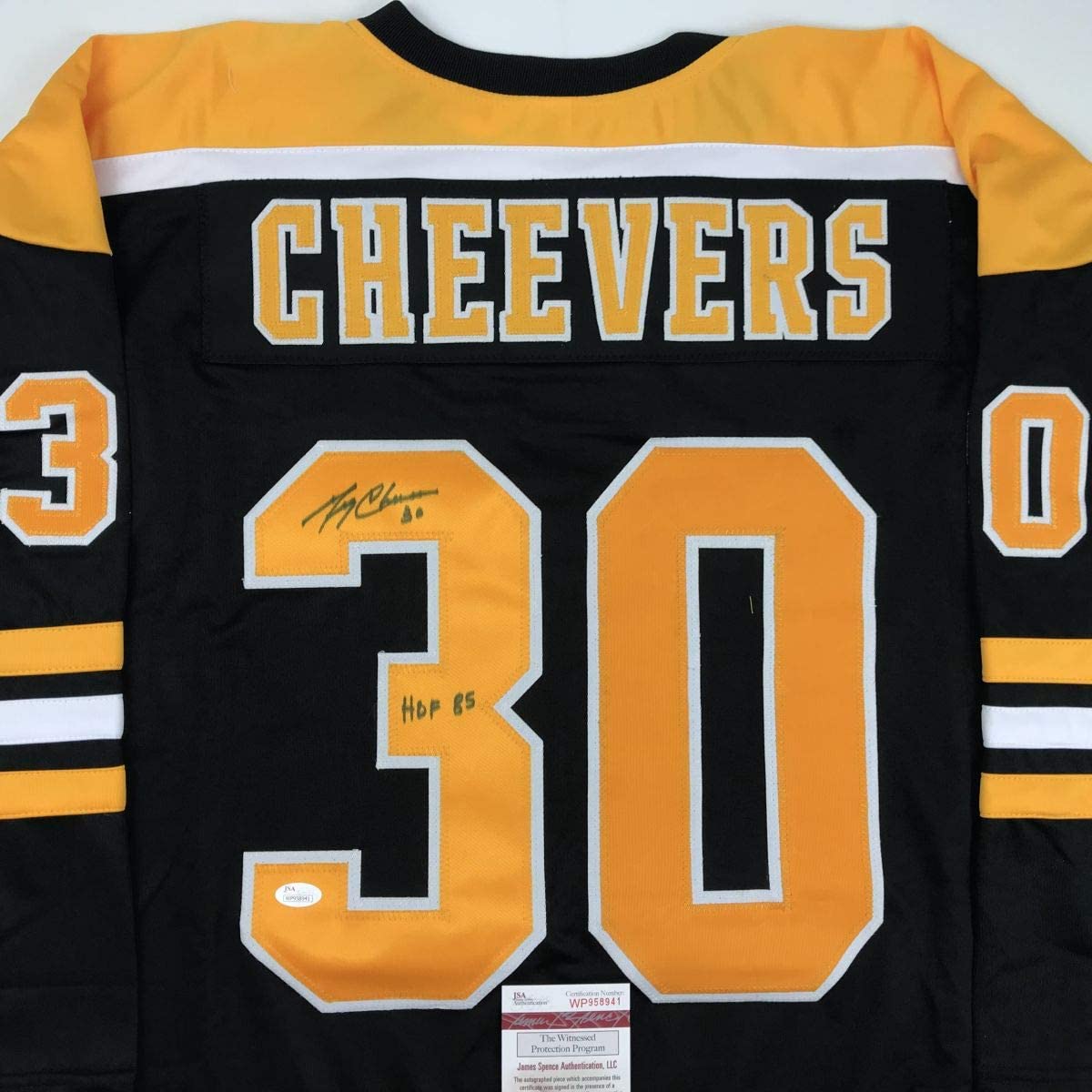 Back view of black and gold Cheevers #30 hockey jersey with signed inscription and HOF 65 notation, showing JSA authentication label at bottom.