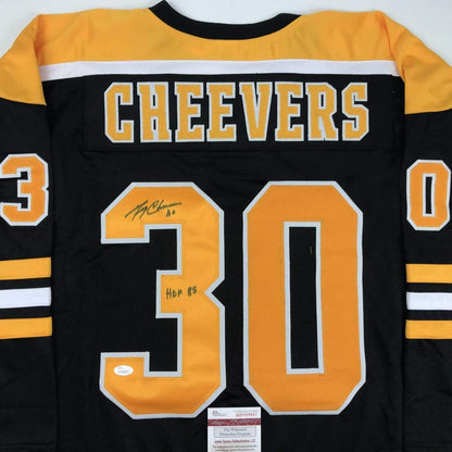 Back view of black and gold Cheevers #30 hockey jersey with signed inscription and HOF 65 notation, showing JSA authentication label at bottom.