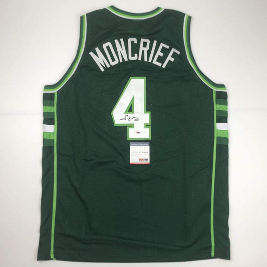 Rear view of dark green basketball jersey with white number 4, "MONCRIEF" text, green trim, and PSA/DNA authentication certificate attached.