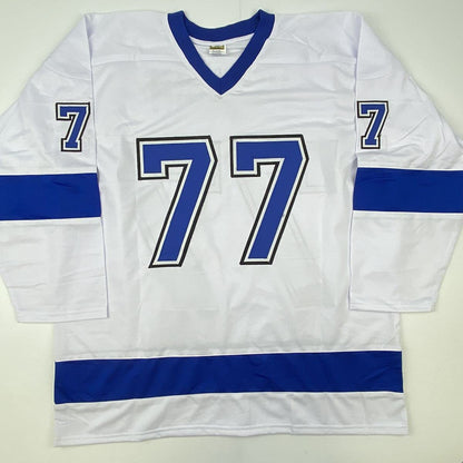 White hockey jersey with blue v-neck collar, blue horizontal stripes, and large blue number 77 with black outline displayed flat on light background.