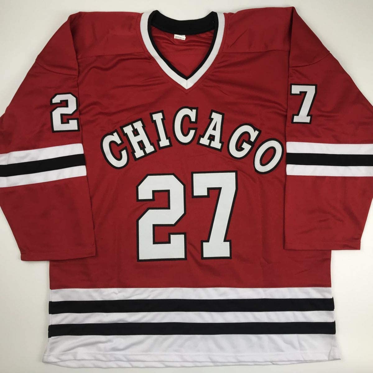 Red Chicago hockey jersey with white and black striped trim, displaying "CHICAGO" and number 27 across chest, laid flat on white background.