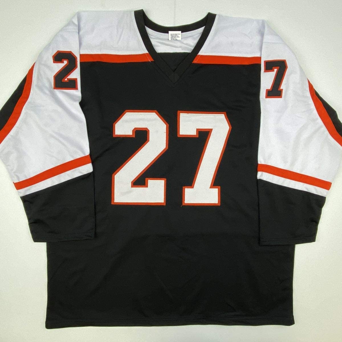 Black hockey jersey with white and red sleeves displaying number 27 in white with red outline, flat lay view.