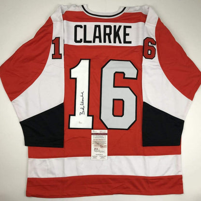 Autographed Philadelphia Flyers jersey #16 with Clarke nameplate, red white and black stripes, displayed flat with JSA authentication certificate visible.