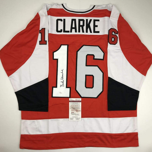 Autographed Philadelphia Flyers jersey #16 with Clarke nameplate, red white and black stripes, displayed flat with JSA authentication certificate visible.