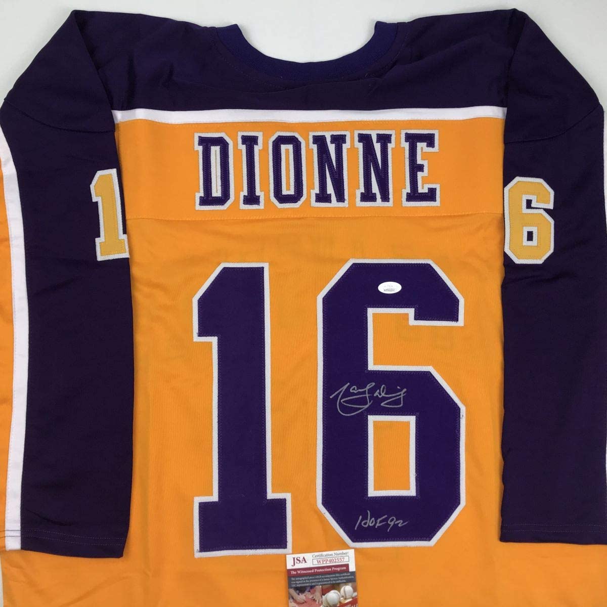 Flat lay of yellow and navy hockey jersey displaying "DIONNE" and number 16 with visible signatures and JSA authentication sticker.