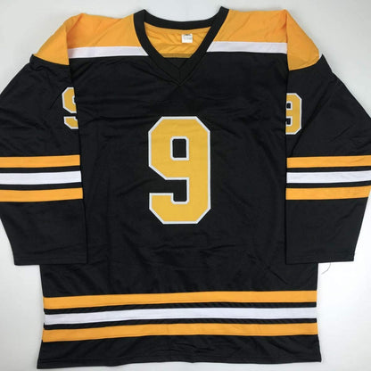 Black hockey jersey with gold and white stripes, featuring large gold number 9 on chest, displayed flat against white background.