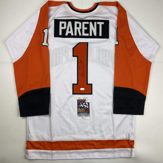 Flat lay of white and orange hockey jersey with "PARENT" and number "1" on back, JSA authentication certificate visible at center.