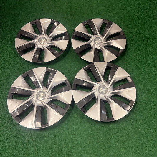 Four two-tone silver and charcoal wheel covers arranged on green surface, showing radial spoke design with center emblems.