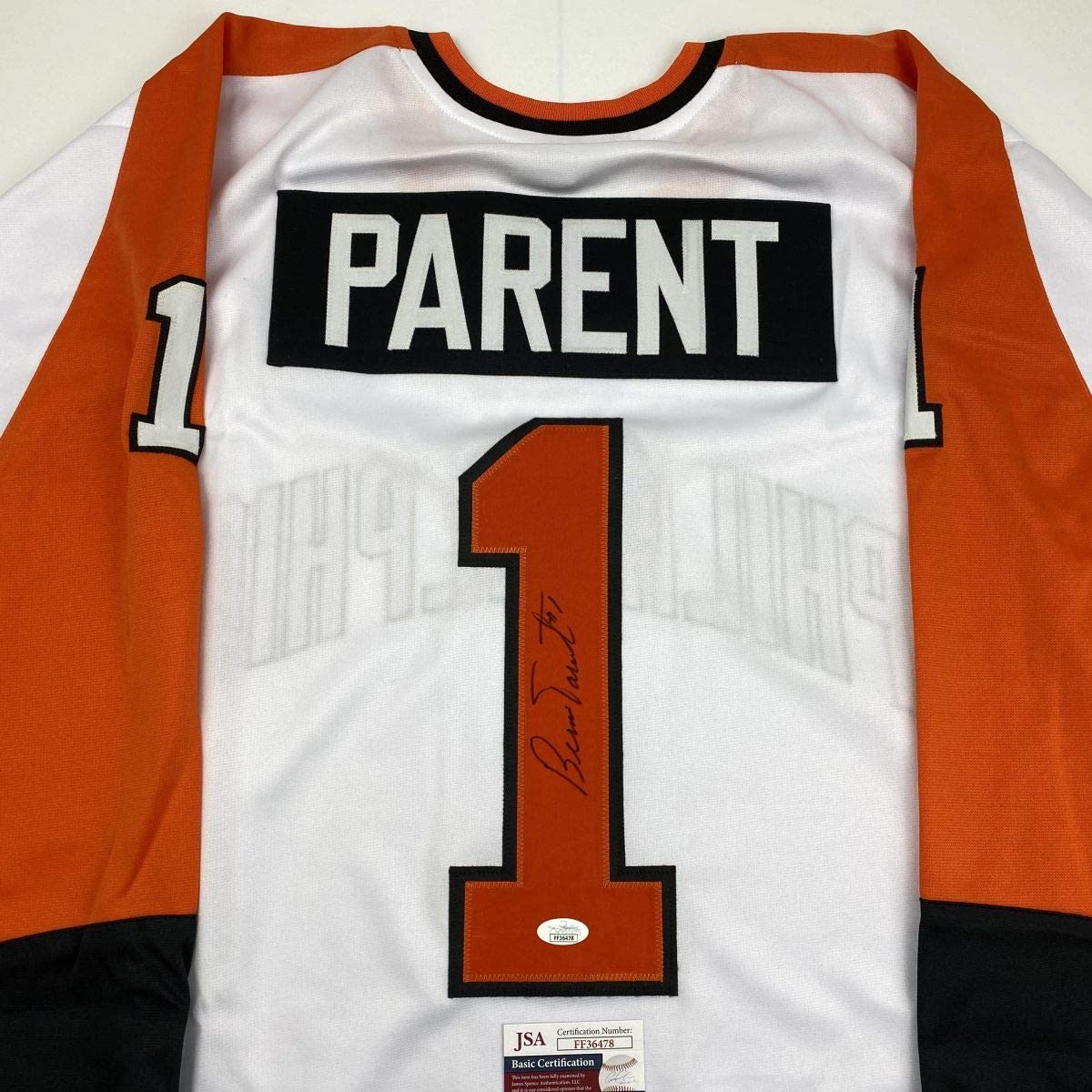 Signed white hockey jersey with orange and black trim displaying "PARENT" nameplate and number 1, with JSA authentication certificate visible at bottom.