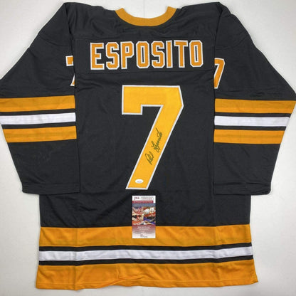 Black Boston Bruins hockey jersey number 7 with "ESPOSITO" across chest, signed in gold pen, displayed flat with JSA authentication certificate visible at bottom.