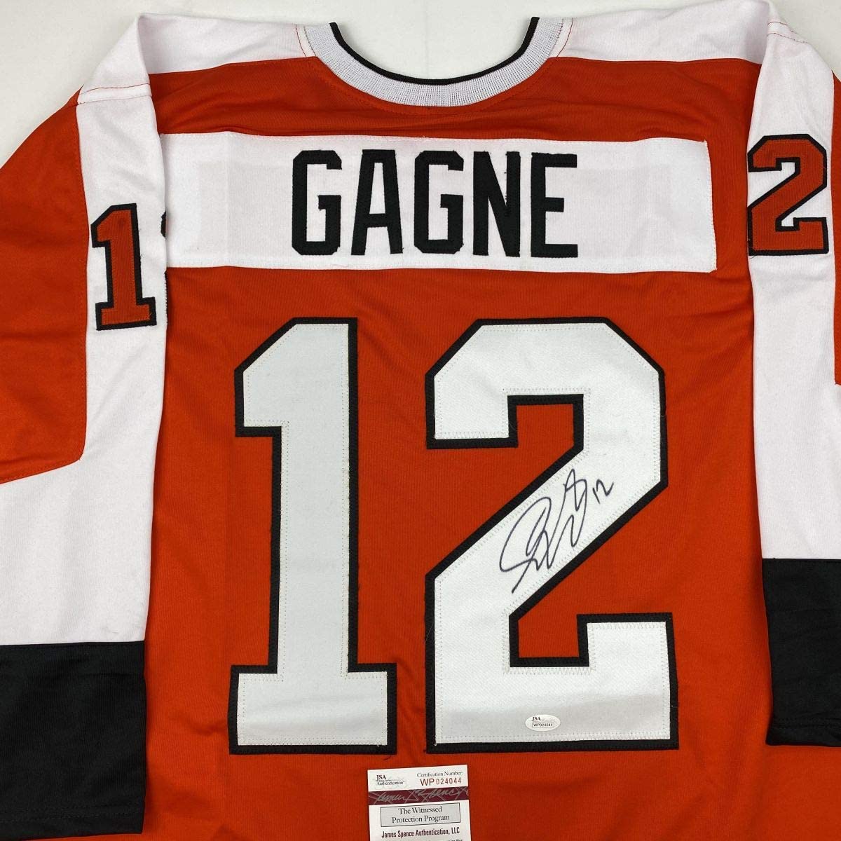 Orange and white Philadelphia Flyers hockey jersey number 12 with "GAGNE" nameplate, signed, displayed flat with JSA authentication label visible.