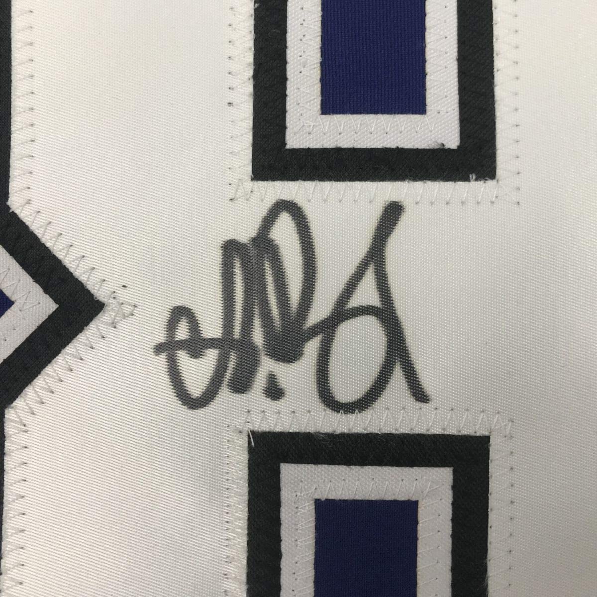 Close-up of handwritten signature on white hockey jersey fabric with navy blue and black geometric design elements.
