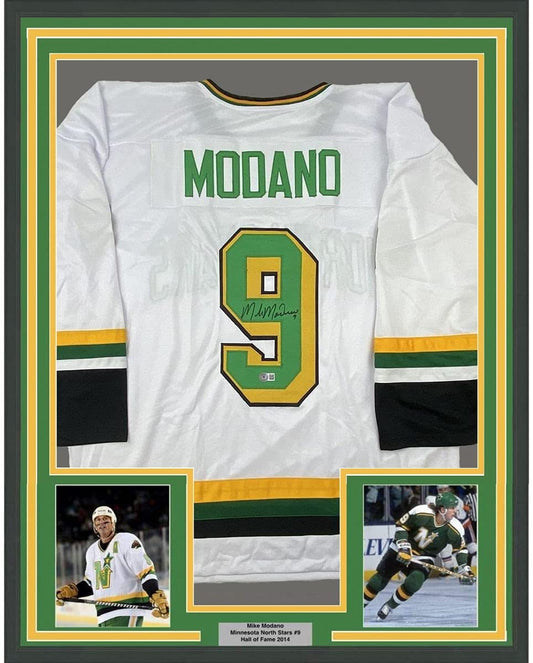 Framed back view of a white hockey jersey with green MODANO lettering, green and gold number 9, and black signature.