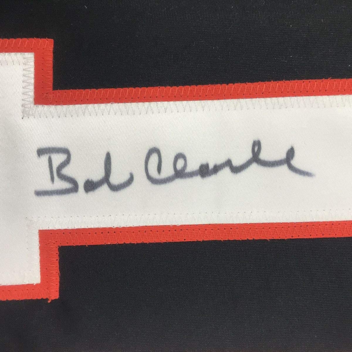 Close-up of handwritten signature "Bob Clarke" on white stripe of red and black hockey jersey.