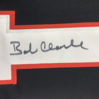 Close-up of handwritten signature "Bob Clarke" on white stripe of red and black hockey jersey.