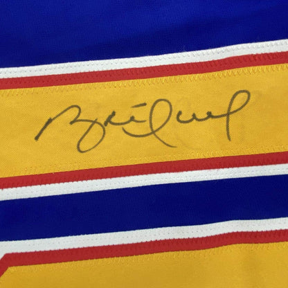 Close-up of handwritten signature on yellow stripe of retro hockey jersey with blue, red, white, and yellow horizontal stripes.