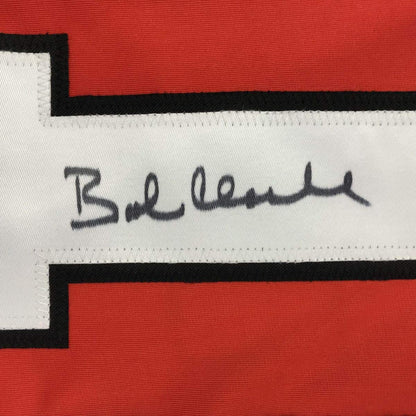 Close-up of handwritten signature "Bob Clarke" in black ink on white stripe of red and black hockey jersey.