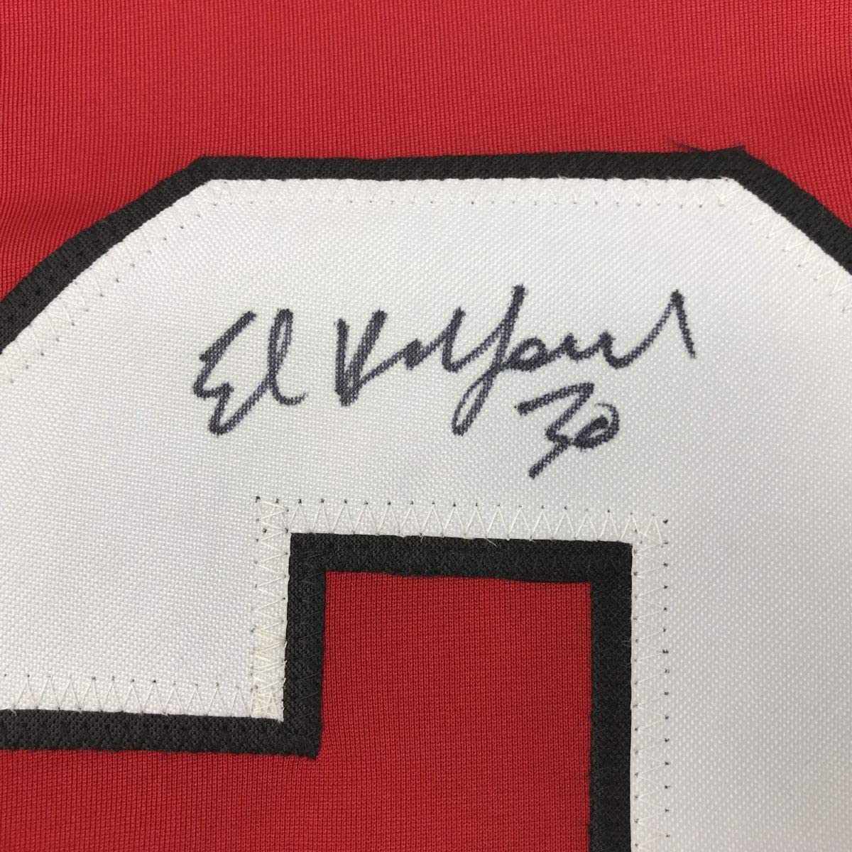 Close-up of handwritten signature "Ed Belfour" with number 72 on white fabric patch with black border against red jersey background.