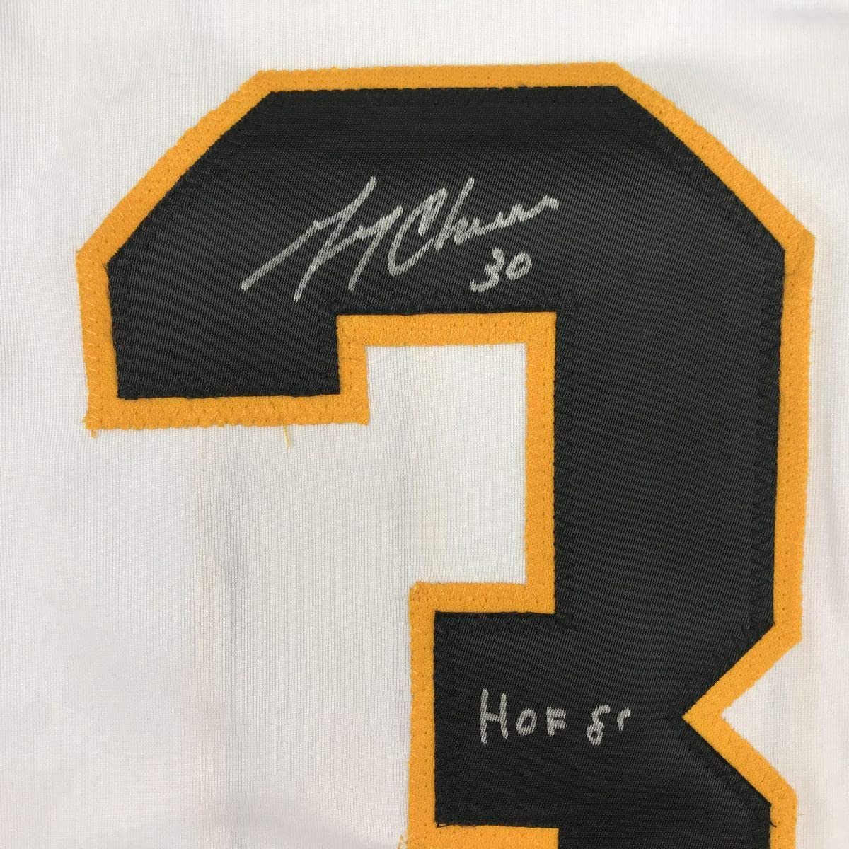 Close-up of black and gold hockey jersey shoulder patch with handwritten signature "Al Dolan 30" and "HOF 85" inscribed in silver pen.