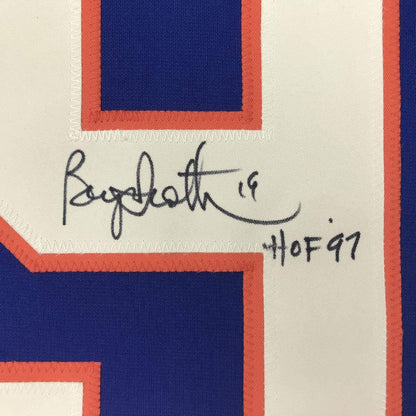 Close-up of handwritten signature "Bryan Trottier '19" and "HOF 97" on cream fabric with red and navy striped jersey border.
